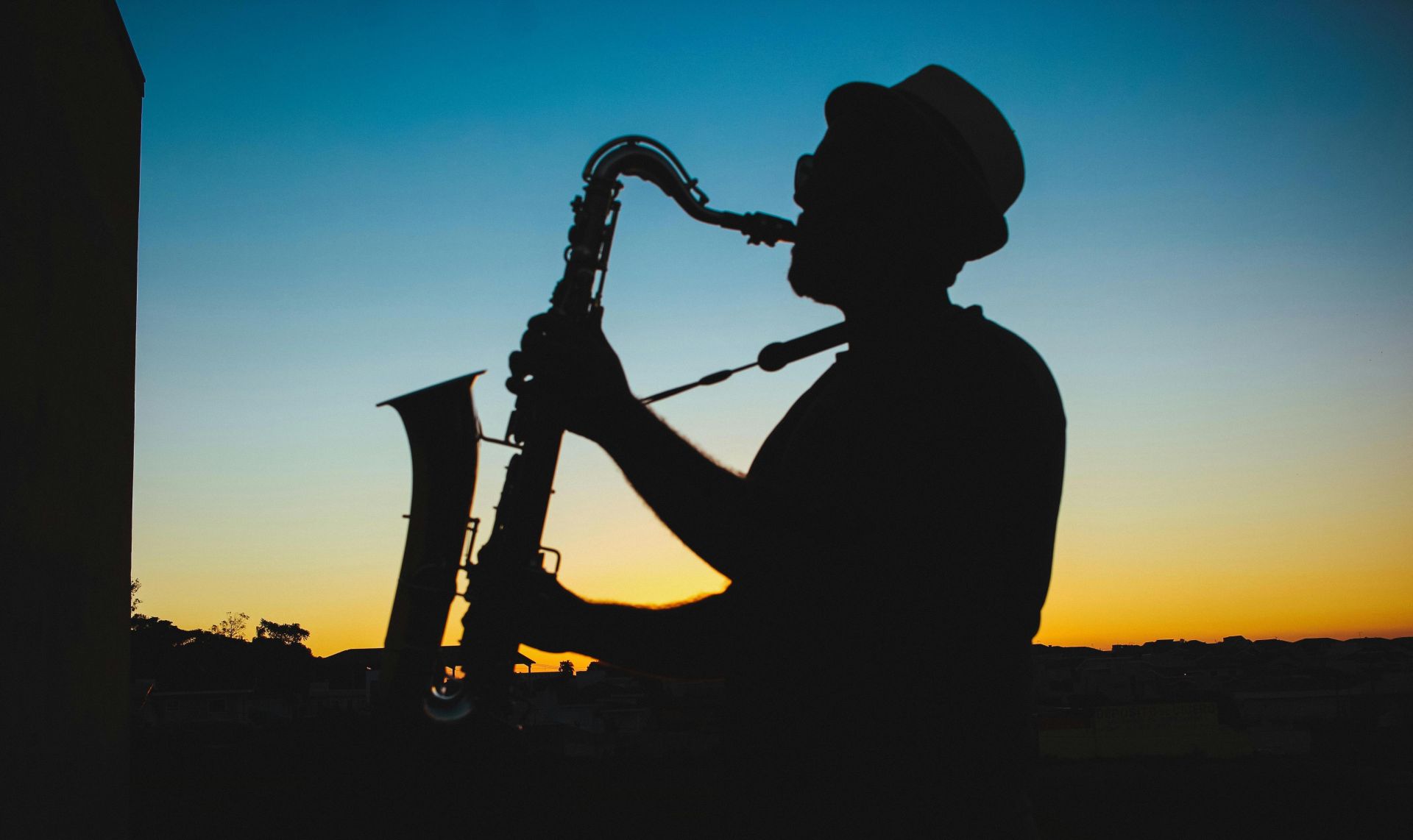 A man playing the saxophone silhouetted against a vibrant sunset sky.